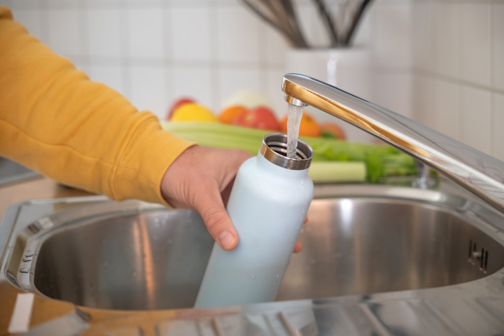 Don't forget to clean the faucet heads too! Inhaling them can help remove accumulated particles. Here, a person is shown filling the water bottle in a sink.